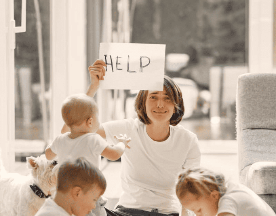 maman solo épuisée qui brandit une feuille sur laquelle est inscrit help
